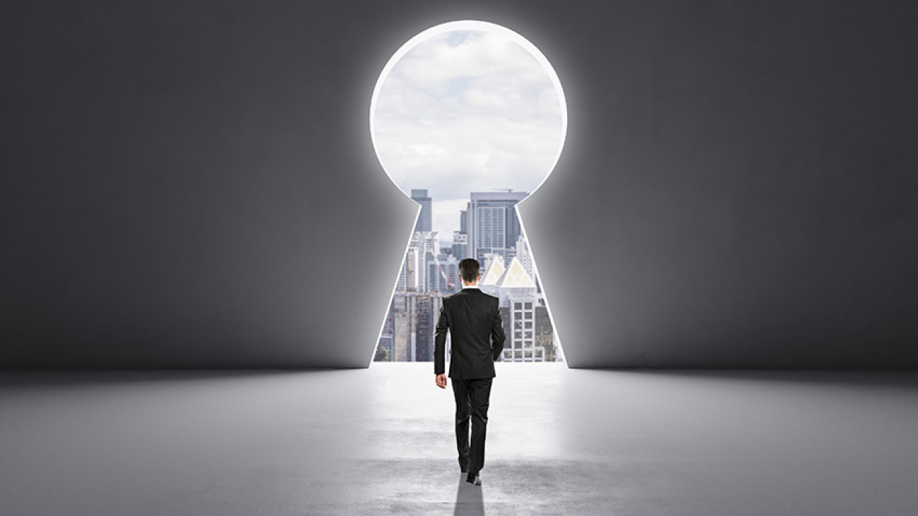 Back view of businessman walking in concrete interior with abstract keyhole window with city view. Key to success and career growth concept. Mock up place